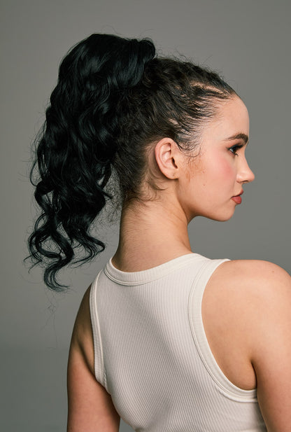 Model wearing the Hebbe ponytail by Ailsa's Wigs – natural black waves styled in a secure high ponytail with bendable metal wrap, viewed from back-right angle.