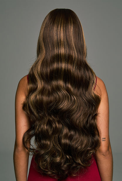 The back view of the Willow 28-inch highlighted mixed brown lace front wig by Ailsa's Wigs. The waves cascade down past the waist, with the honey-brown highlights sparkling under the sunlight, creating a playful yet elegant vibe.